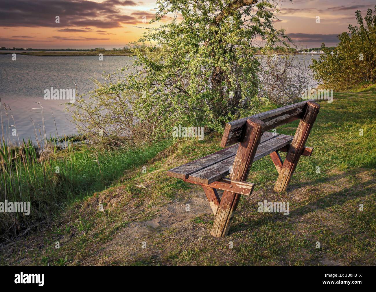 Eine Bank am ruhigen Lagunenufer bei Sonnenuntergang, ein Ort, an dem Gedanken und Träume sanft landen. Stockfoto