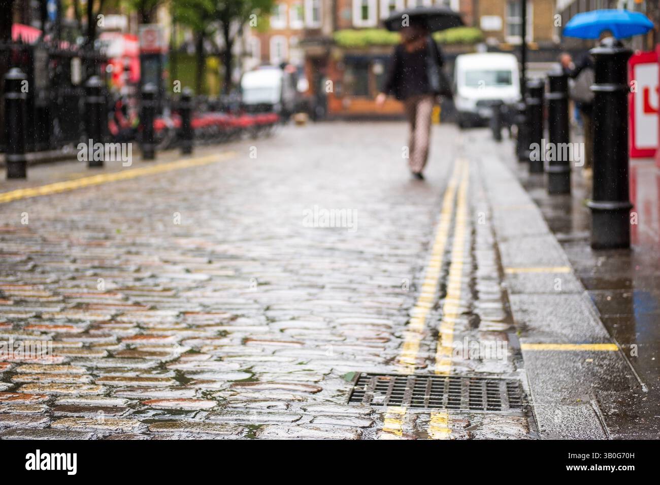 Nahe fokussierte Straße mit Kopfsteinpflaster in London Soho mit einer Person, die einen Schirm im Hintergrund trägt, und Platz für Textkopien Stockfoto