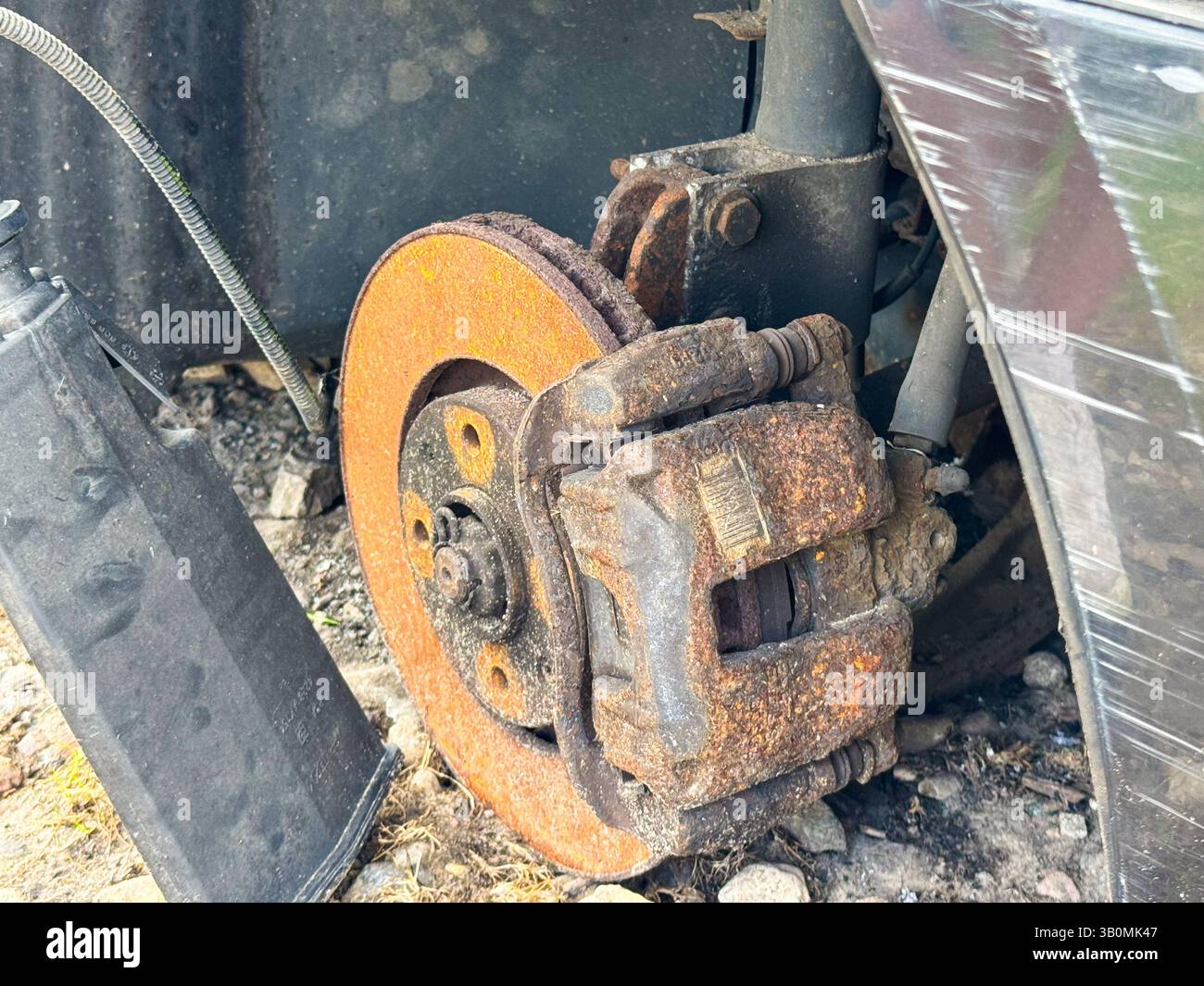 Verrostete Bremssattel und Bremsscheibe eines Fahrzeugs mit starker Korrosion am Bremssystem, freiliegende Aufhängungskomponenten und Radnabenbaugruppe. Stockfoto