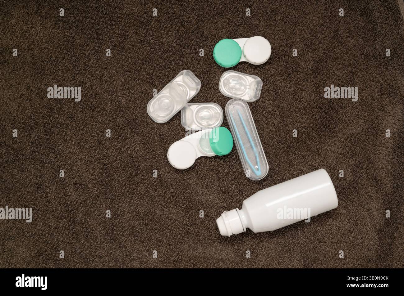 Eine lebendige Kollektion von Kontaktlinsenbehältern und einer Lösungsflasche, elegant auf einem weichen Handtuchhintergrund angeordnet Stockfoto