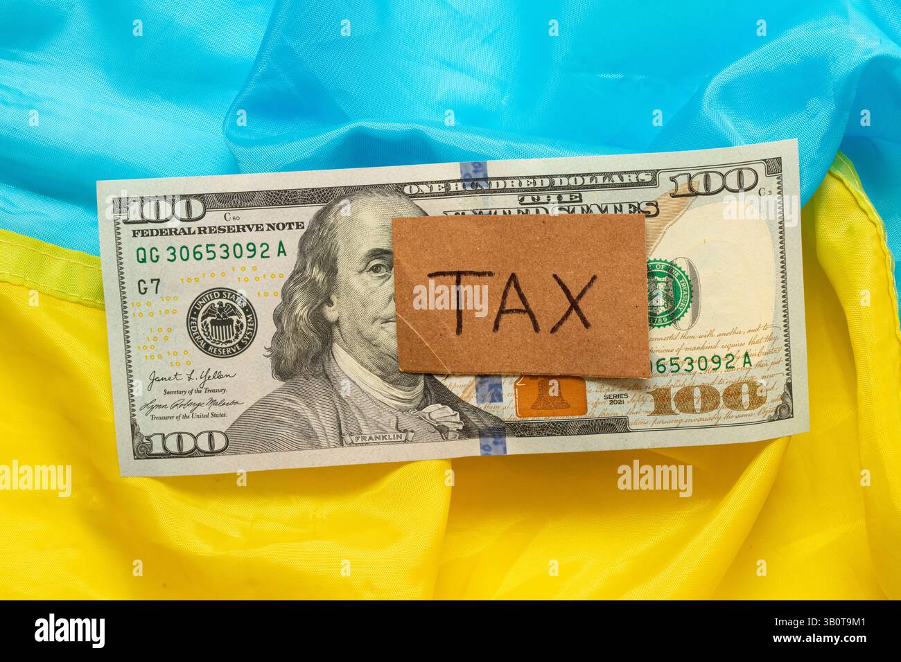 Die Inschriftsteuer auf einem Stück Pappe, der US-Dollar und die Flagge der Ukraine, das Konzept der Steuerpolitik, Inflation und Zölle Stockfoto