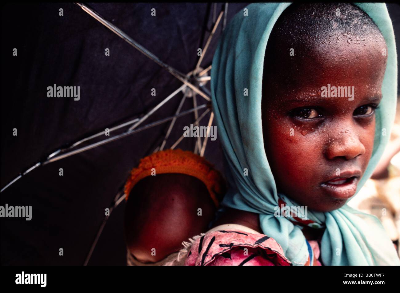 Ein junges Mädchen mit ihrer kleinen Schwester auf dem Rücken trägt einen Regenschirm, um die Sonne in der extremen Hitze des Tages abzuwehren, Tecumbia, Eritrea, Juni 1983 Stockfoto