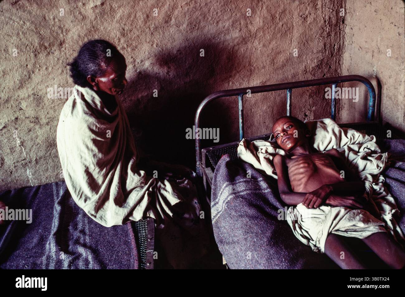 Ein kleiner Junge mit Tuberkulose in einem Krankenhausbett, der von seiner Mutter, dem ländlichen Eritrea, Juine 1983, besucht wird Stockfoto