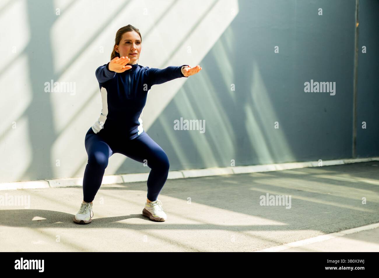 Eine Frau führt ein konzentriertes Workout durch und führt in einem hell beleuchteten Fitnessraum mit Entschlossenheit Squats aus. Stockfoto