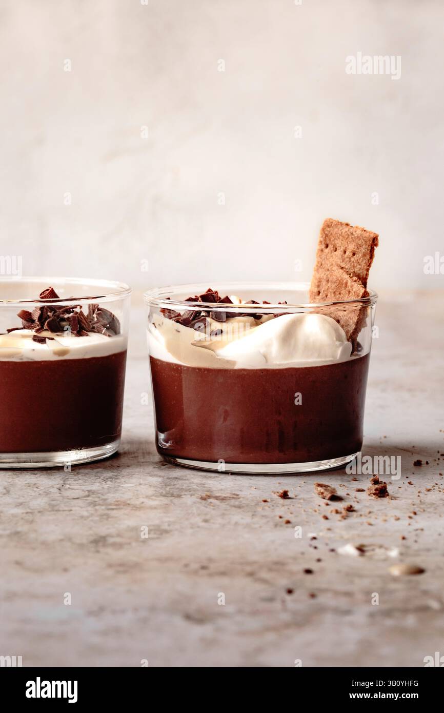 Zwei Glasbecher gefüllt mit Schokoladenmousse mit Schlagsahne, Schokoraspeln und einem Keks. Stockfoto