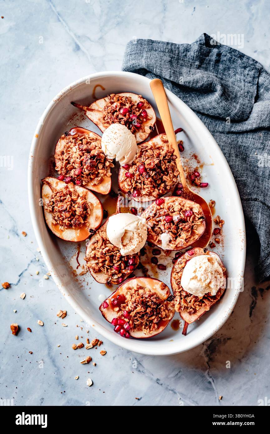 Gebackene Birnen mit Granola-Streusel und Eis, serviert auf einem weißen ovalen Gericht. Stockfoto