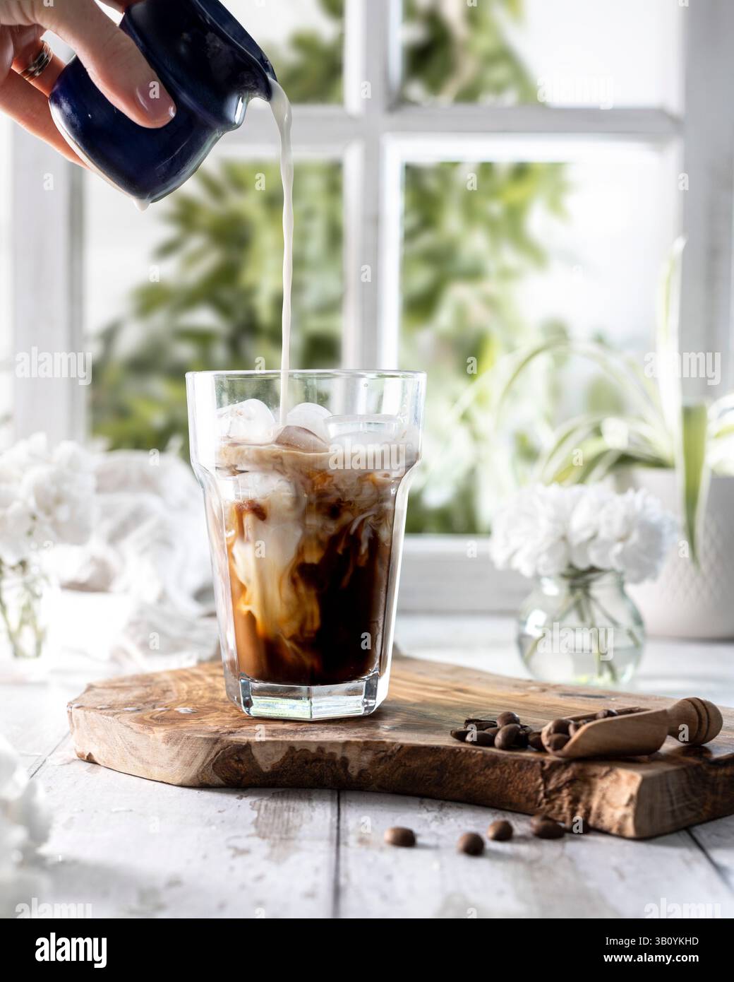 Eiskaffee in einem Glas mit einer Hand, die Milch eingießt Stockfoto
