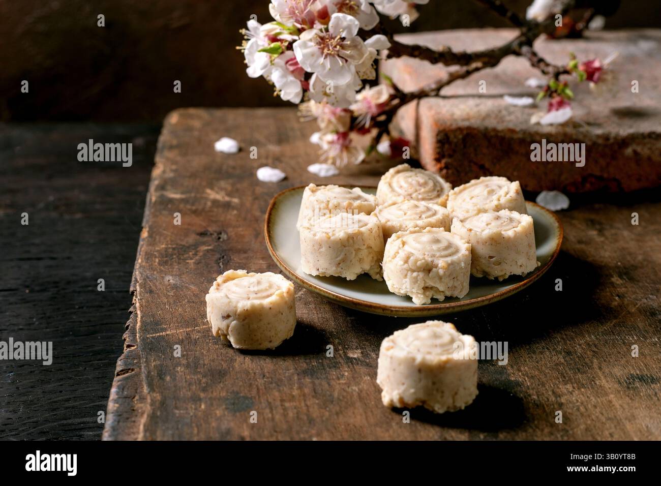 Traditionelles asiatisches Dessert Süßigkeiten Sesamcreme auf Keramikplatte. Rustikaler Holztisch mit Kirschblütenzweig dekoriert. Hausgemachtes Reismehl Stockfoto
