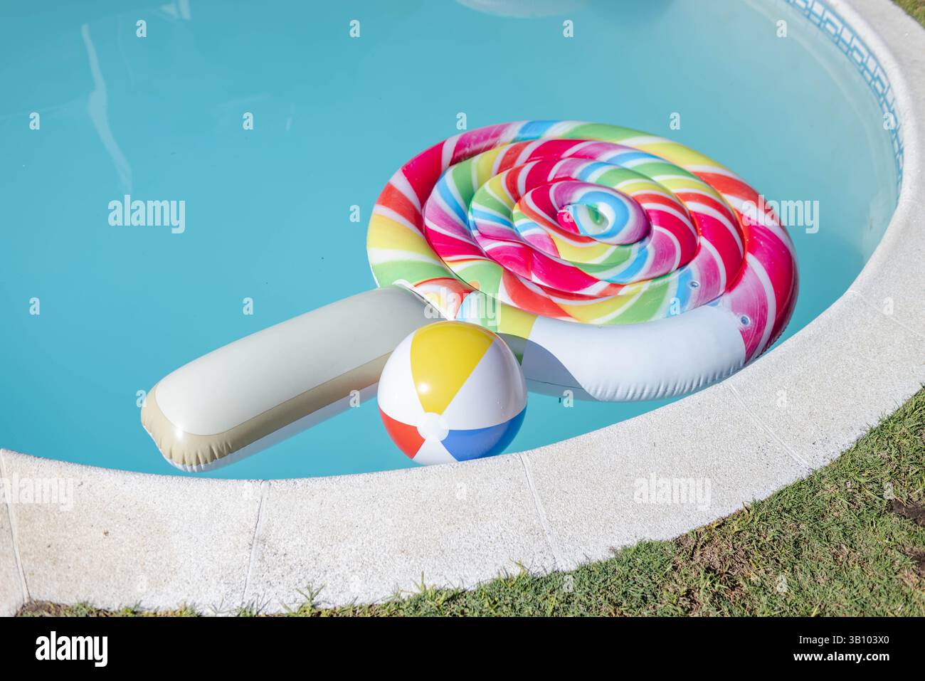 Farbenfrohes, in Lutscher gewirbeltes Schwimmer im Hinterhof-Pool mit buntem Strandball Stockfoto