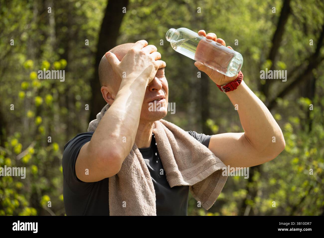 Sportlicher Erwachsener kaukasier erfrischt sich bei Sommerhitze Wasser aus der Flasche gegen Wald nach dem Training im Freien. Wasserhaushalt. Hitzegefahr. Ove Stockfoto