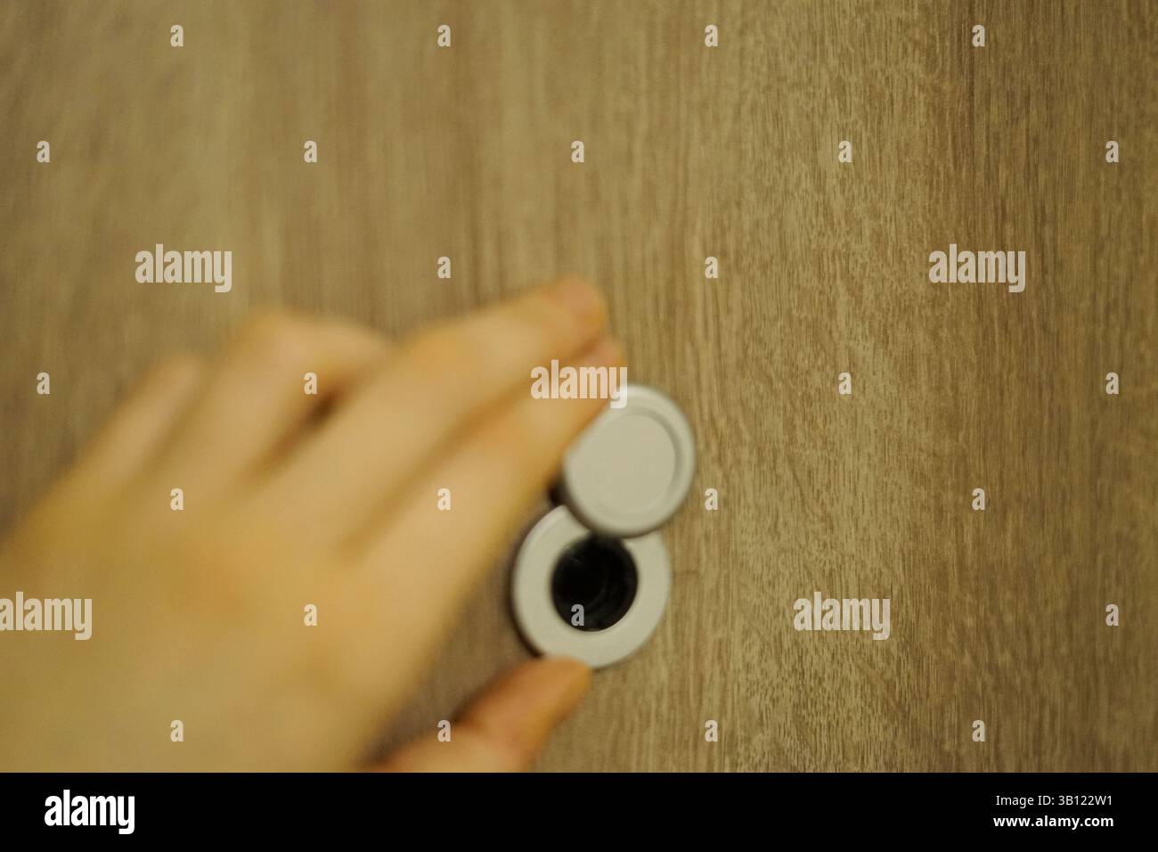 Nahaufnahme der Frau Hand öffnet Metall-Peephole Abdeckung Holztür Privatsphäre Sicherheit und Schutz Stockfoto