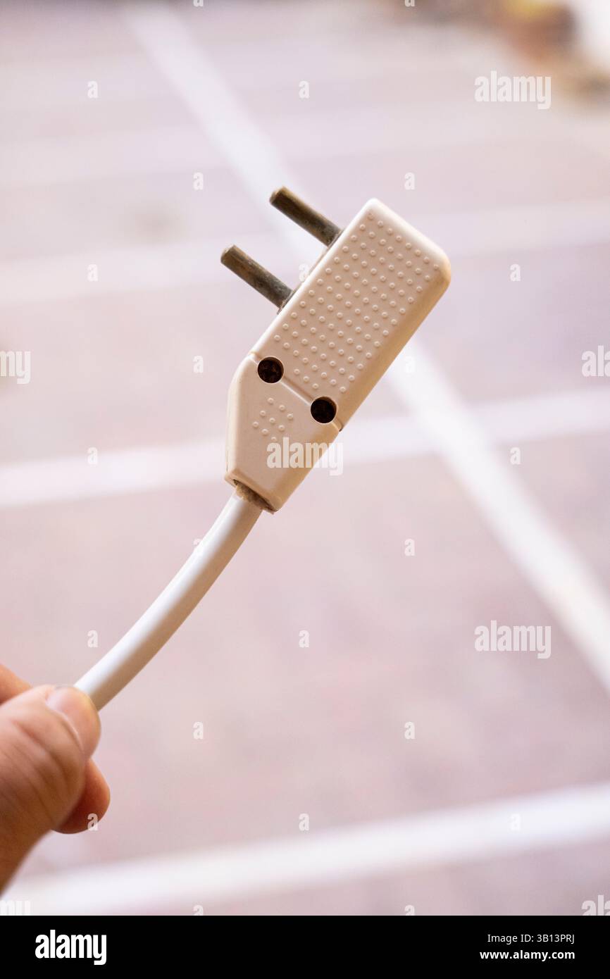 Eine minimalistische Nahaufnahme eines zweipoligen Steckers, gehalten oder schwebend mit verschwommenem Hintergrund. Perfekt zur Illustration elektrischer Geräte, Connectio Stockfoto