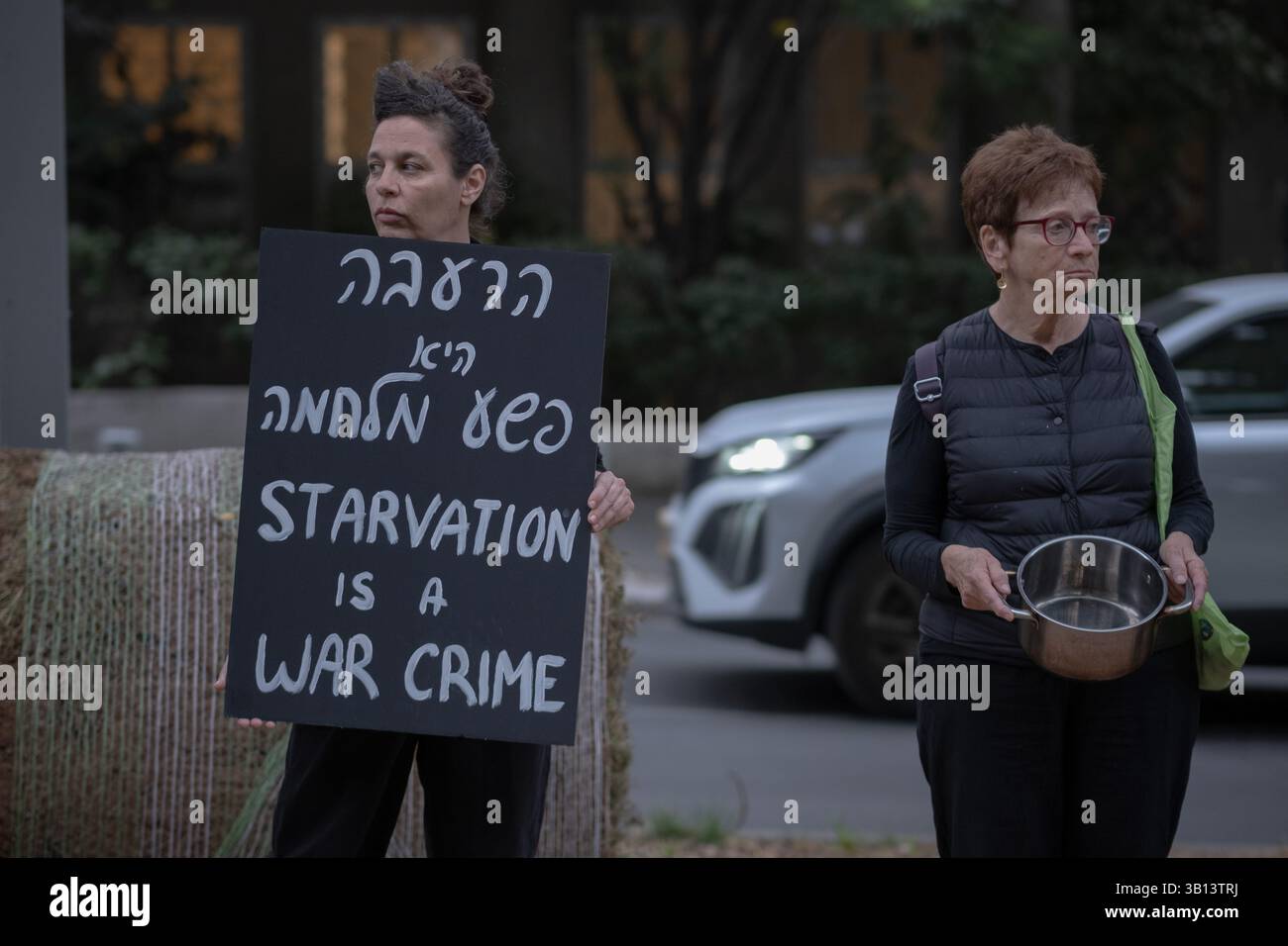 Tel Aviv, Tel Aviv, Israel. April 2025. Eine Frau mit einem Schild mit der Aufschrift "Hunger ist ein Kriegsverbrechen" und eine andere hält einen leeren Topf, um gegen den Hunger in Gaza zu protestieren. (Kreditbild: © Gaby Schuetze/ZUMA Press Wire) NUR REDAKTIONELLE VERWENDUNG! Nicht für kommerzielle ZWECKE! Stockfoto