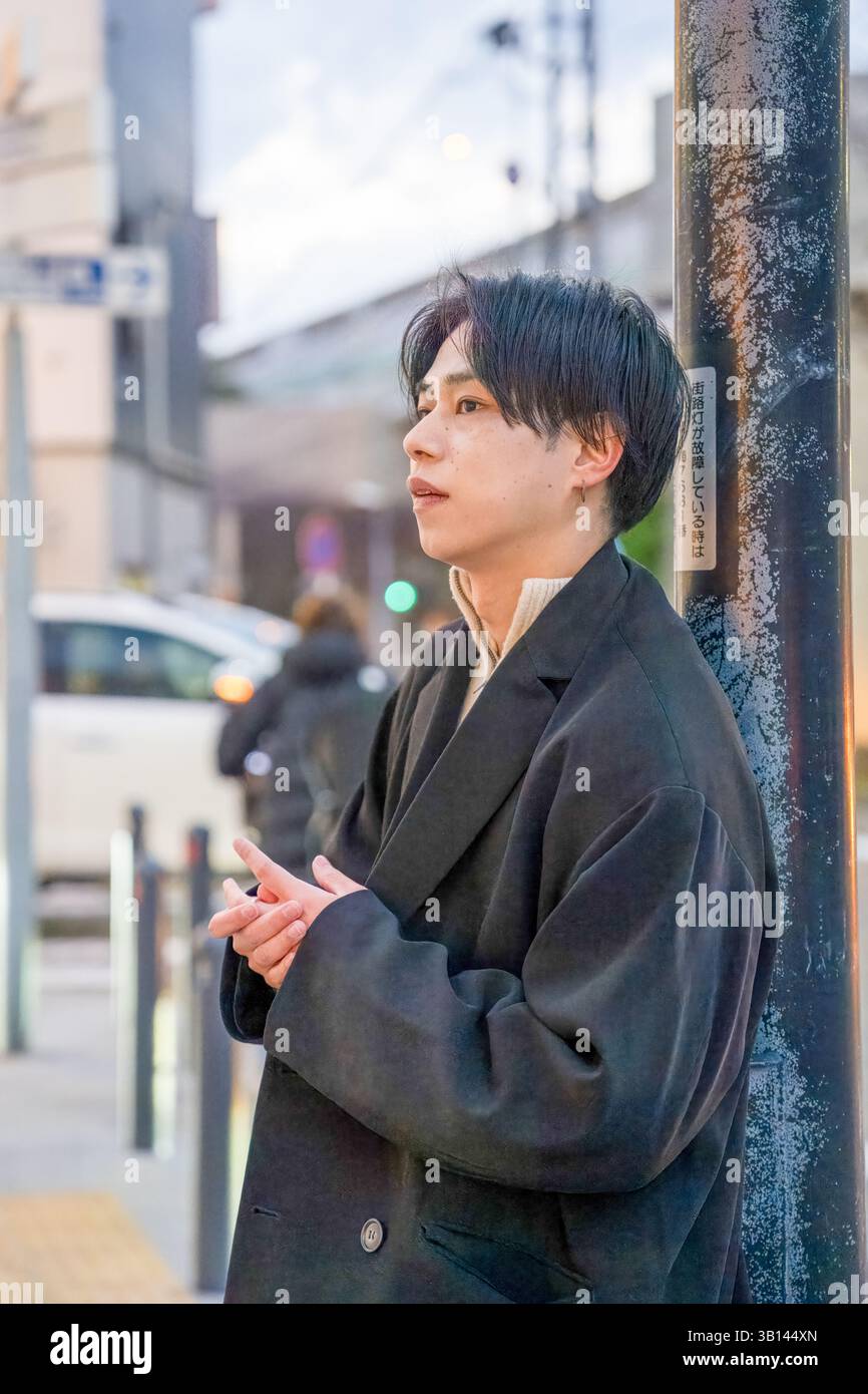 Ein Japaner in seinen Zwanzigern, der eine schwarze Jacke trägt, ist in Minato Mirai, Yokohama, Präfektur Kanagawa. Er steht an einer Straßenkreuzung im Eveni Stockfoto