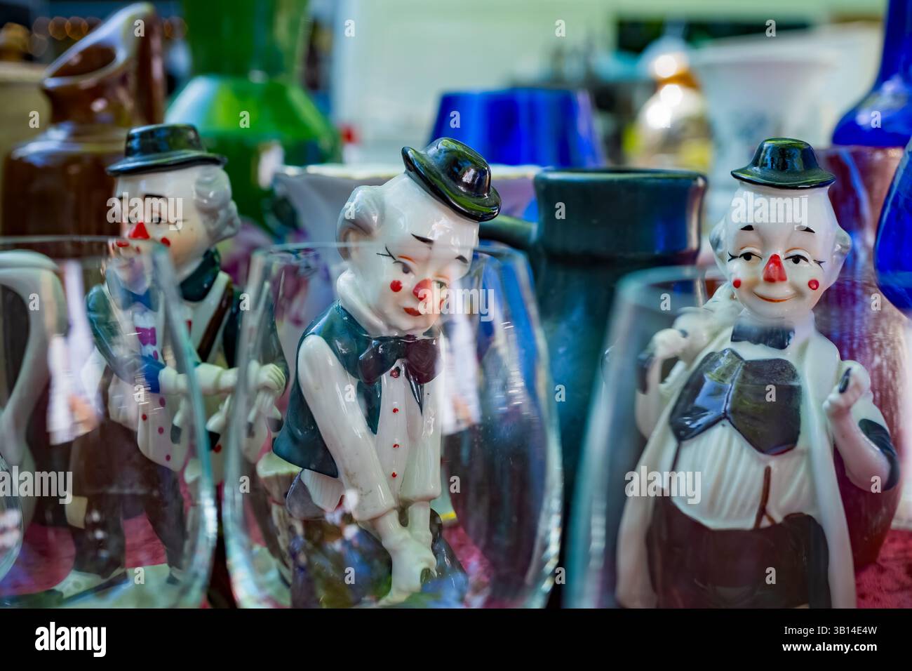 Porzellan-Clown-Figuren zwischen alten Glaswaren an einem farbenfrohen Berliner Flohmarkt, voller Vintage-Charme und Nostalgie. Stockfoto