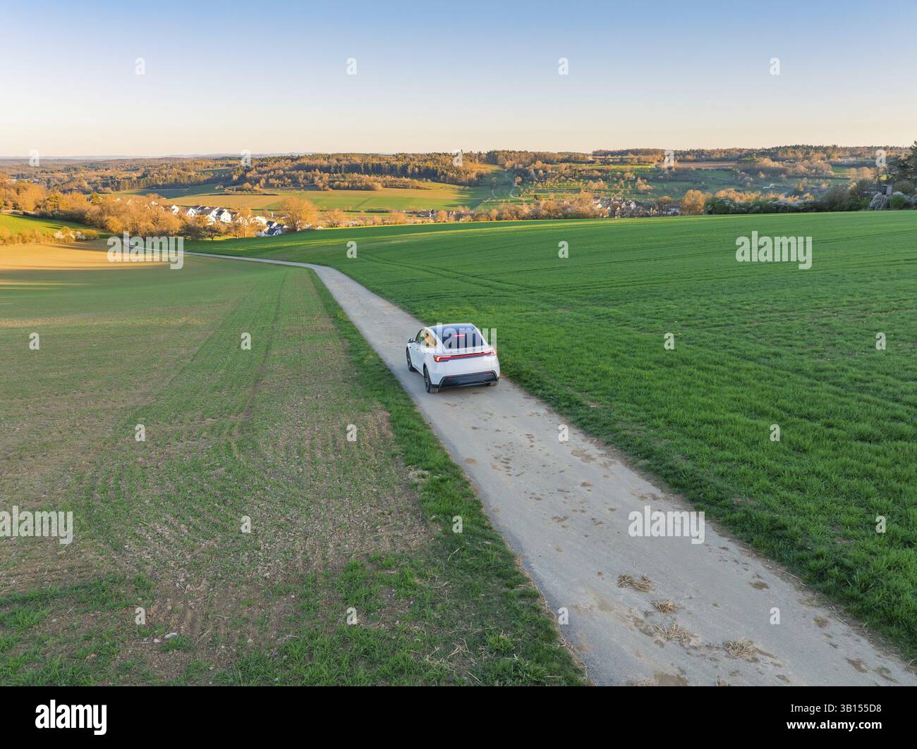 Ein Panoramablick auf ein Auto auf einer Straße, umgeben von endlosen Feldern in der Abendsonne, Tesla, New Model Y, Schwarzwald, Deutschland, Europa Stockfoto