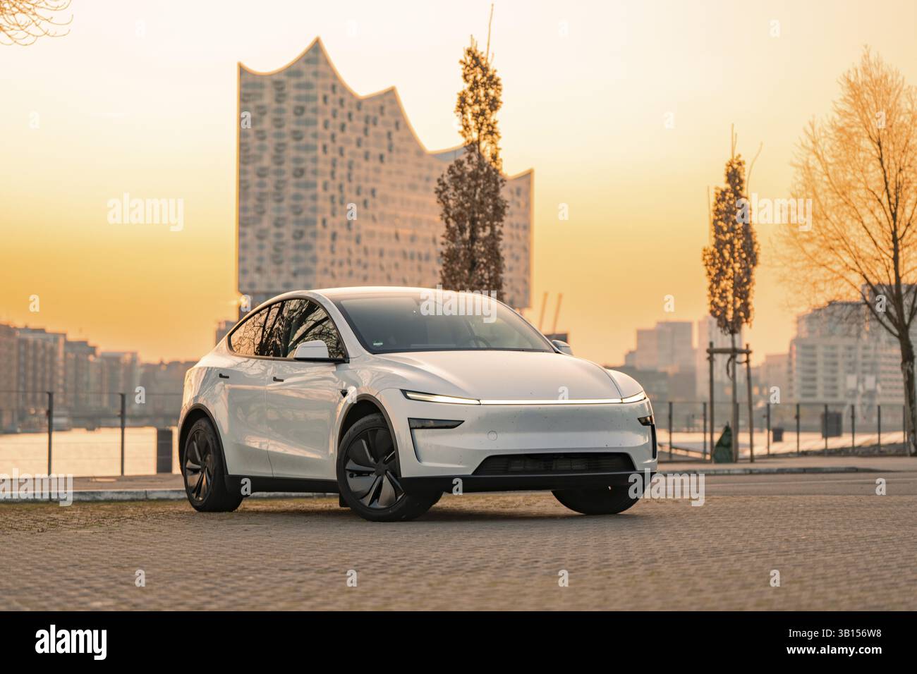 Weißes Elektroauto vor einem modernen Gebäude bei Sonnenuntergang in der Stadt, Tesla New Model Y, Deutschland, Europa Stockfoto