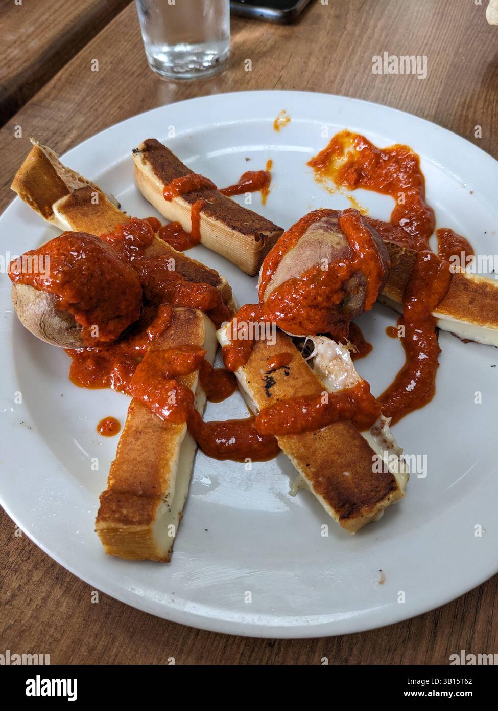 Ein Teller mit gegrilltem halloumi-Käse, Kartoffeln und anderem Gemüse, garniert mit einer aromatischen roten Sauce, perfekt für eine Mahlzeit. Stockfoto