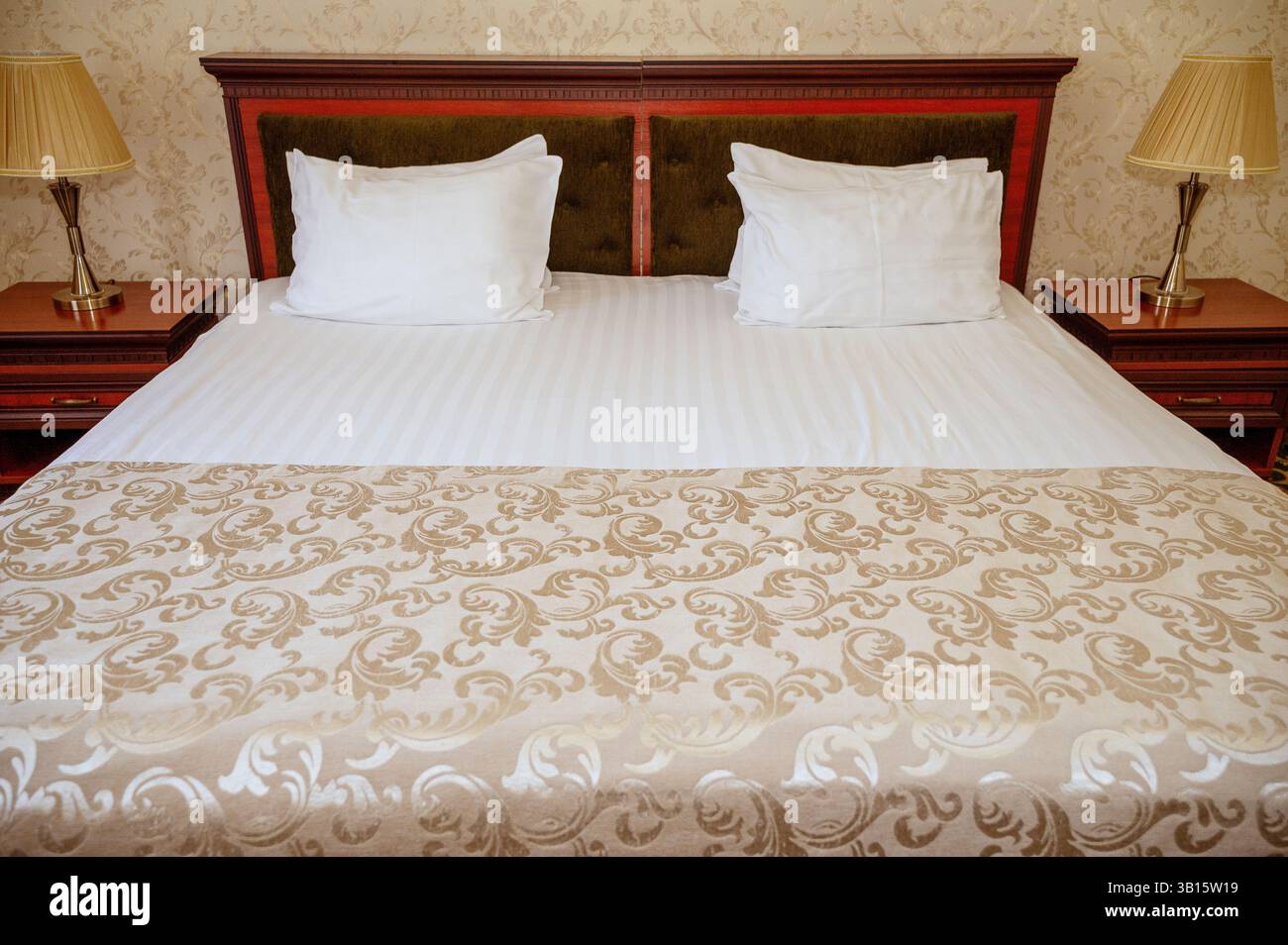 Doppelbett mit dunkelrotem Holz, Kopfteil, sauberer weißer Bettwäsche und Kissen Stockfoto