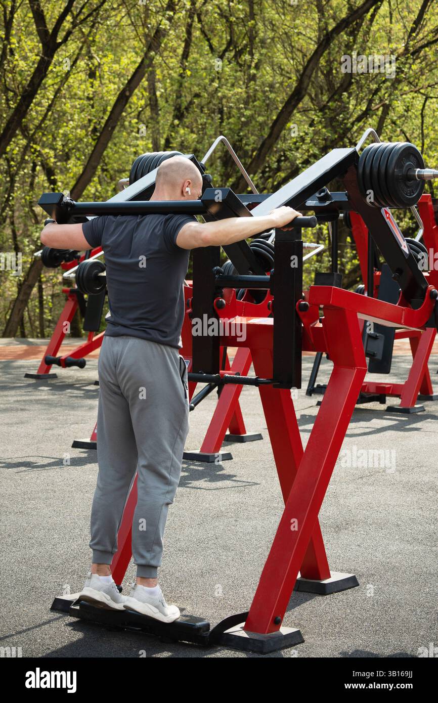 Männliche Athleten üben Krafttraining im Freien mit einer Beinpresse mit Gewichten aus. Der Mann zeigt Entschlossenheit während seines Trainings. Open Air. Stockfoto