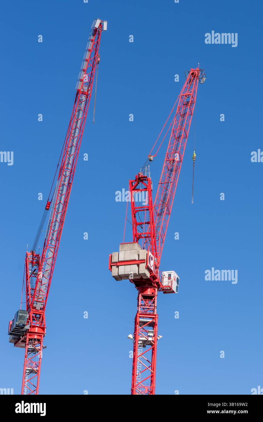 Es gibt zwei große rote Baukräne, die vor einem hellblauen Himmel stehen Stockfoto