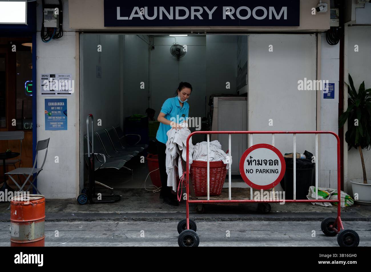 Die weibliche Arbeiterin sortiert frische Wäsche vor einem schnörkellosen Wäscheraum Stockfoto