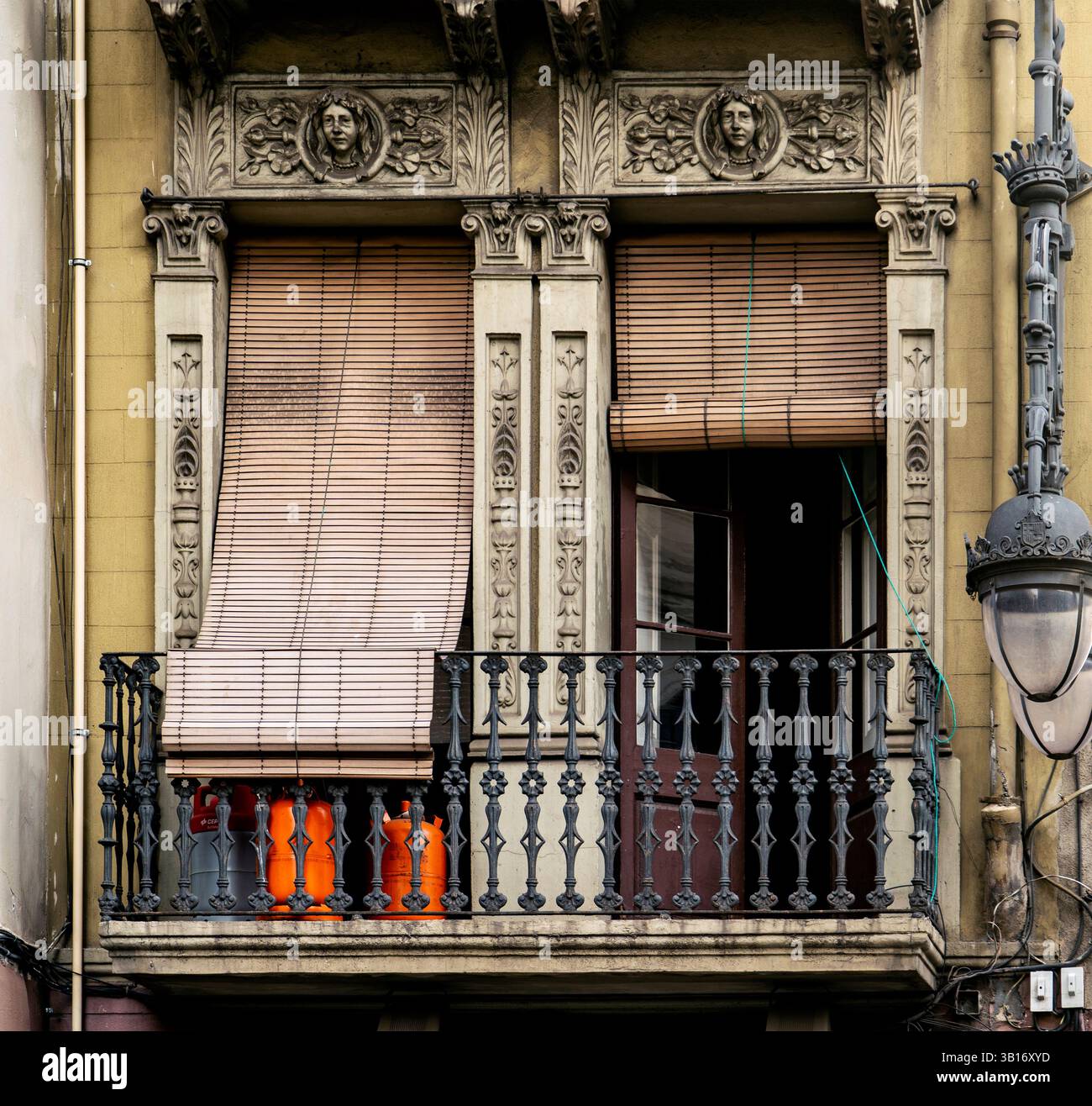 Ein detaillierter Blick auf einen reich verzierten Balkon mit dekorativen Steinarbeiten und Holzjalousien. Der Balkon verfügt über ein schmiedeeisernes Geländer und zwei orangene Vasen. Th Stockfoto