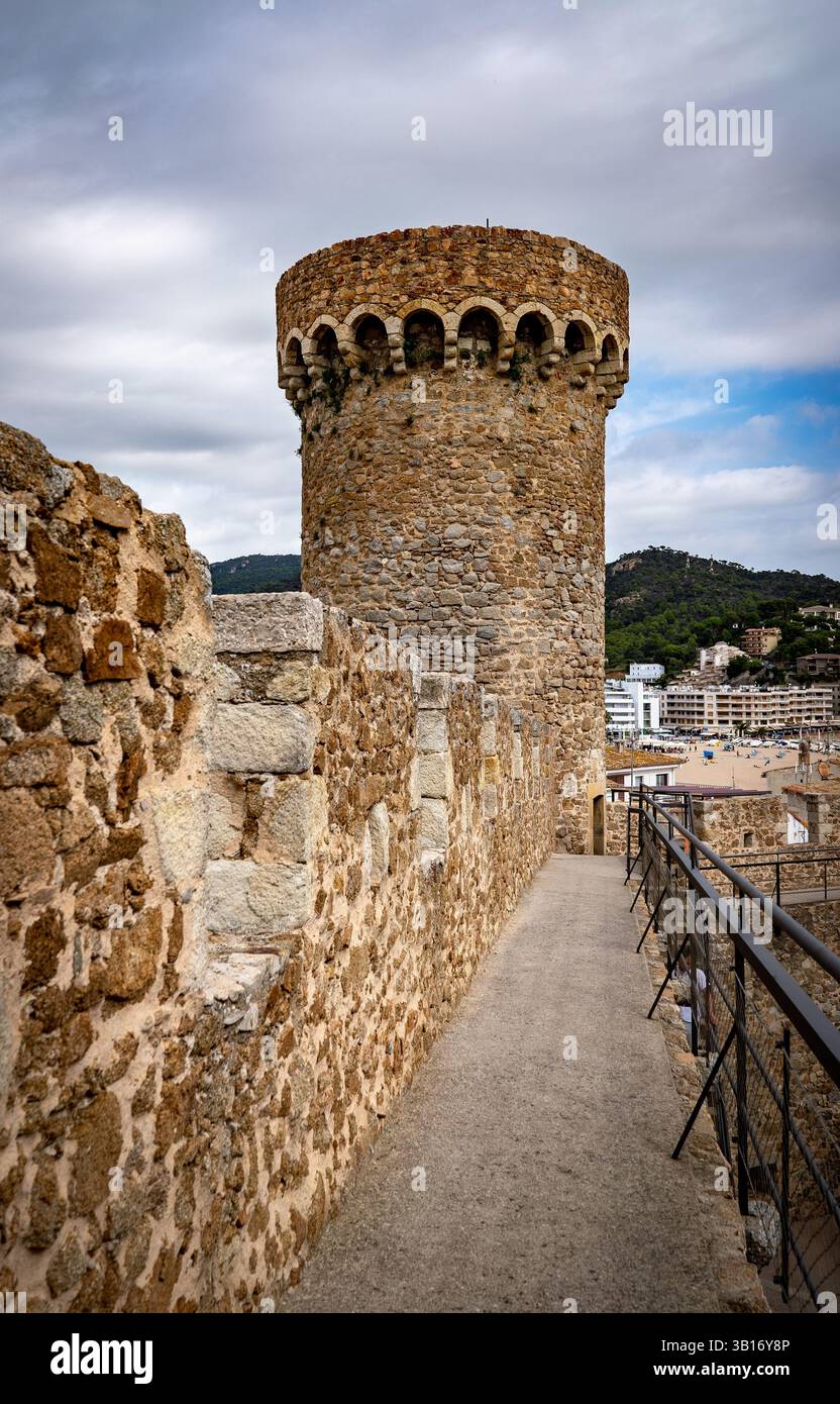 Ein historischer Steinturm mit einer runden Spitze, umgeben von einer mittelalterlichen Mauer. Die Szene zeigt einen Gang, der zum Turm führt, mit einer Kulisse aus Modern Stockfoto