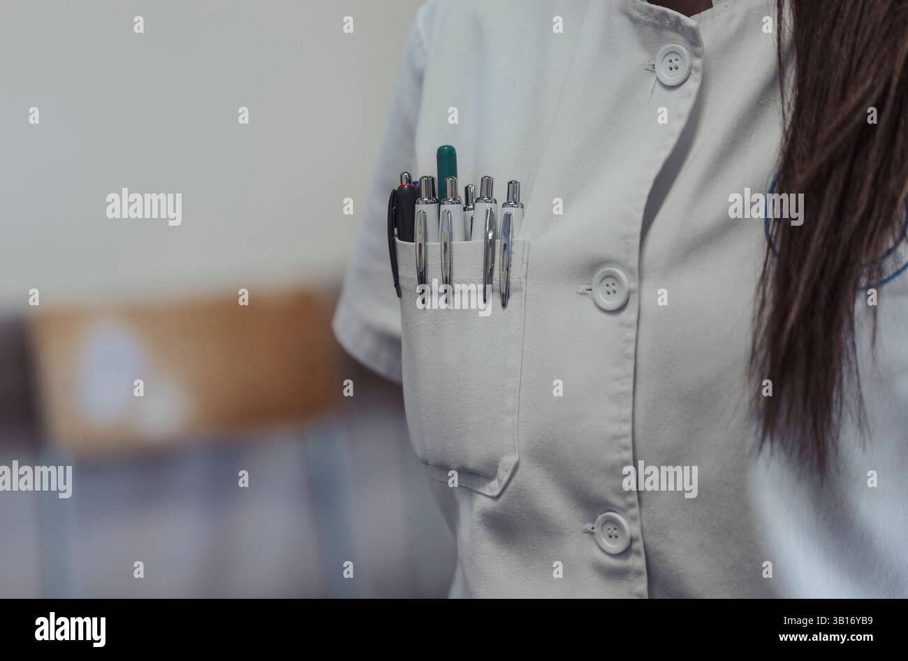 Eine Frau mit weißem Mantel steht selbstbewusst, mit mehreren Stiften in der Tasche ihrer Uniform, was auf das berufliche Umfeld hinweist Stockfoto