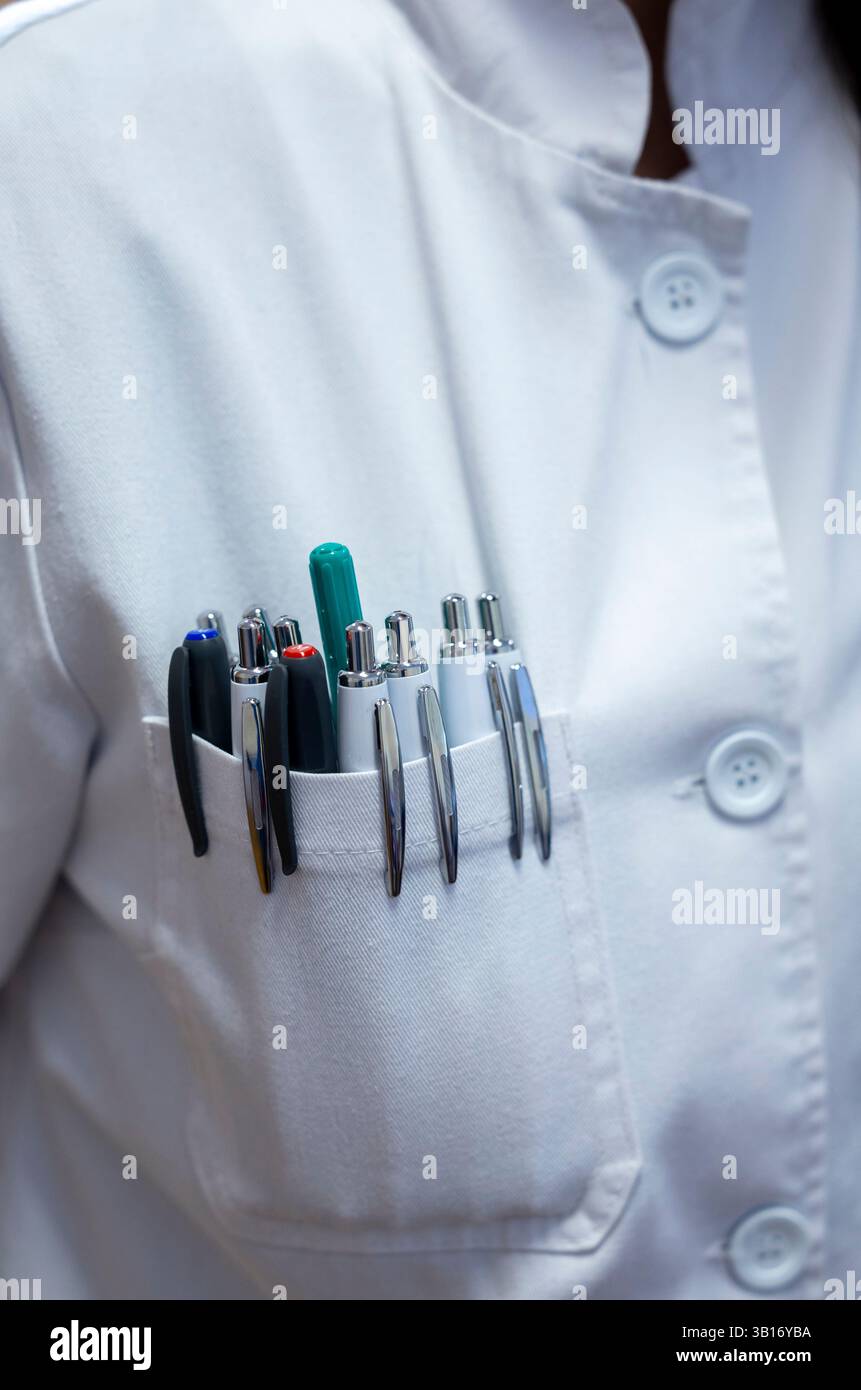 Eine Frau mit weißem Mantel steht selbstbewusst, mit mehreren Stiften in der Tasche ihrer Uniform, was auf das berufliche Umfeld hinweist Stockfoto