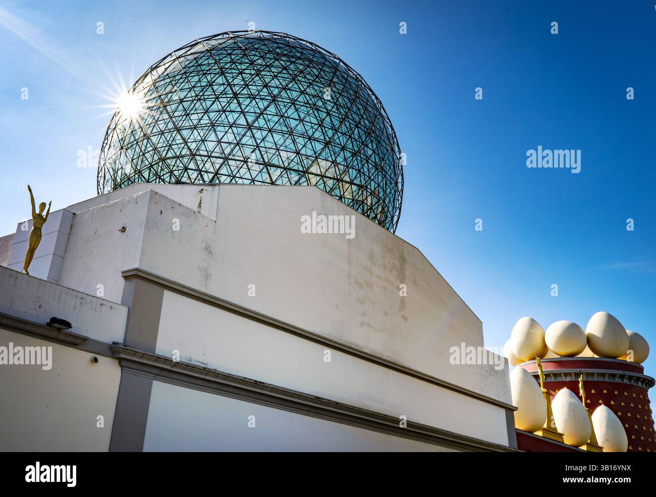 Eine moderne architektonische Struktur mit einer geodätischen Glaskuppel und künstlerischen Elementen unter einem klaren blauen Himmel. Stockfoto