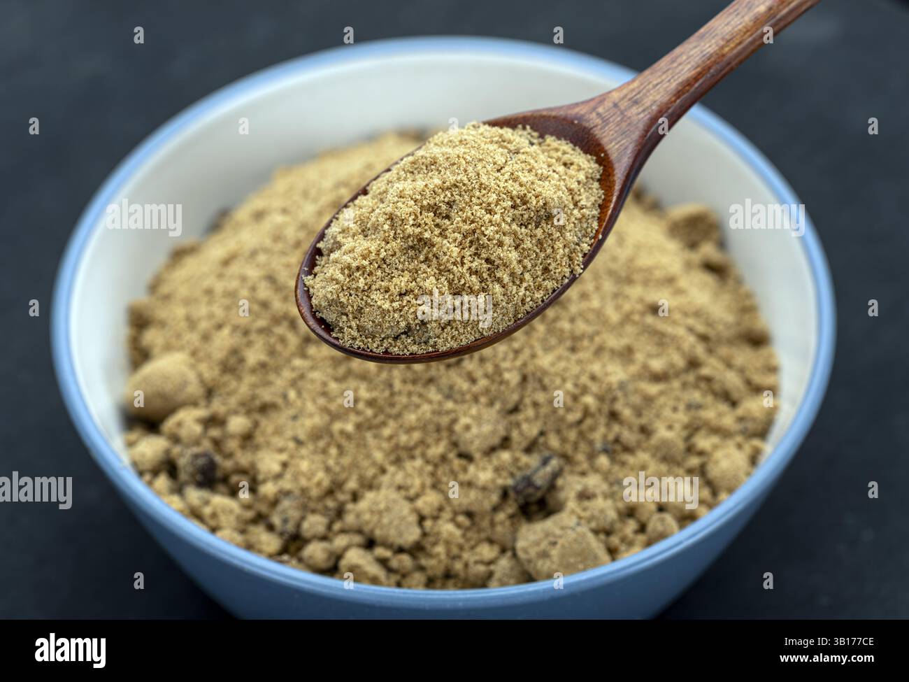 Bio Brown Sugar: Eine Nahaufnahme fängt die reichhaltige Textur und das einladende Aroma von Bio-braunem Zucker ein, präsentiert in einer rustikalen Schüssel und einem Holzlöffel. Stockfoto