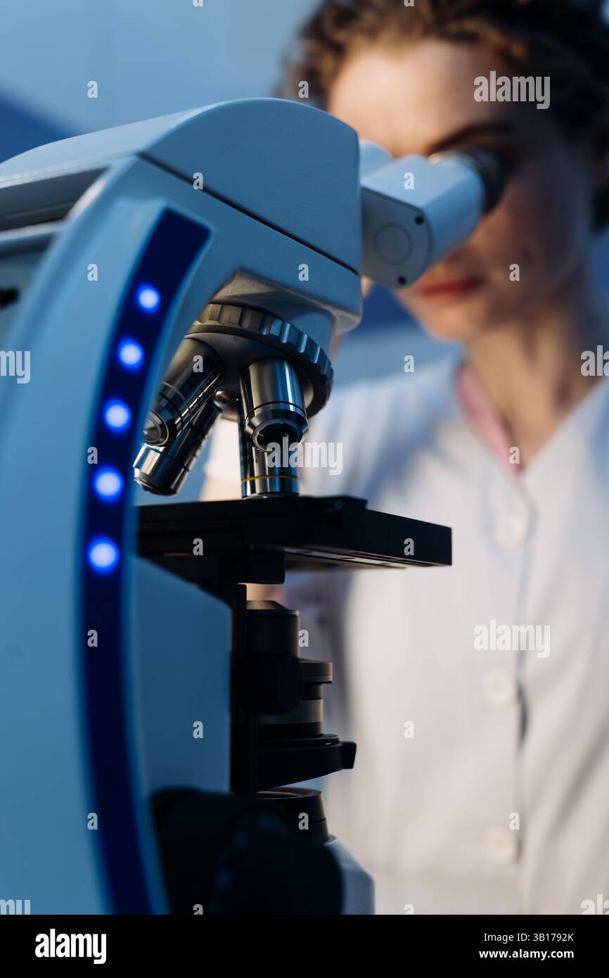 Wissenschaftlerin in steriler Kleidung, die am Tisch sitzt und Forschungsuntersuchungen in einem medizinischen Labor mit einem Mikroskop durchführt. Mikrobiologie Stockfoto