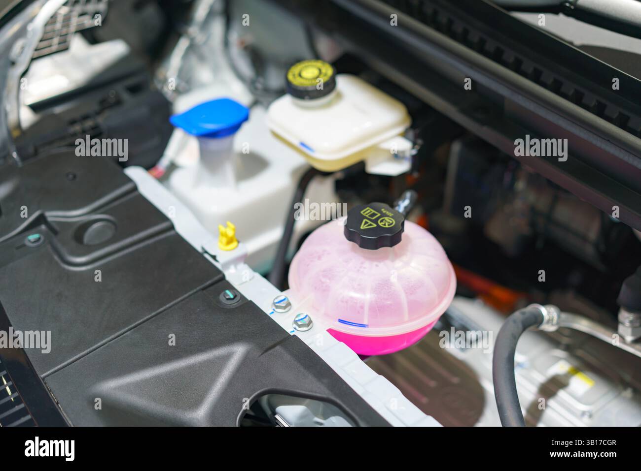 Ein Blick aus nächster Nähe unter der Motorhaube eines modernen Elektrofahrzeugs, der die Kühlmittel- und Flüssigkeitsbehälter hervorhebt, die für eine effiziente Fahrzeugleistung und wartung unerlässlich sind Stockfoto
