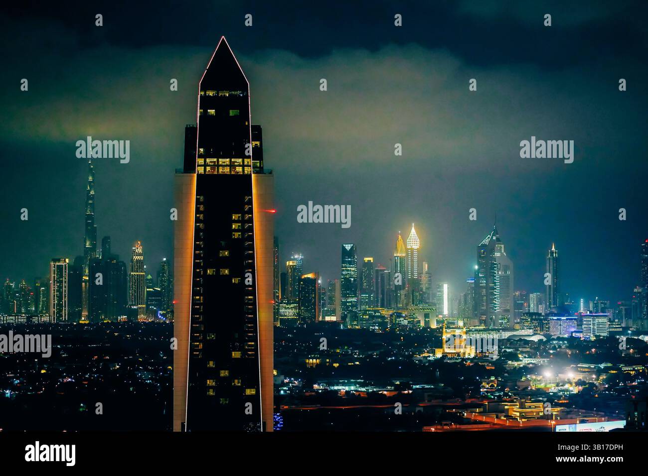 Die beleuchtete Skyline von Dubai bei Nacht mit dem Burj Khalifa und anderen prominenten Wolkenkratzern unter einem dramatischen, bewölkten Himmel. Stockfoto