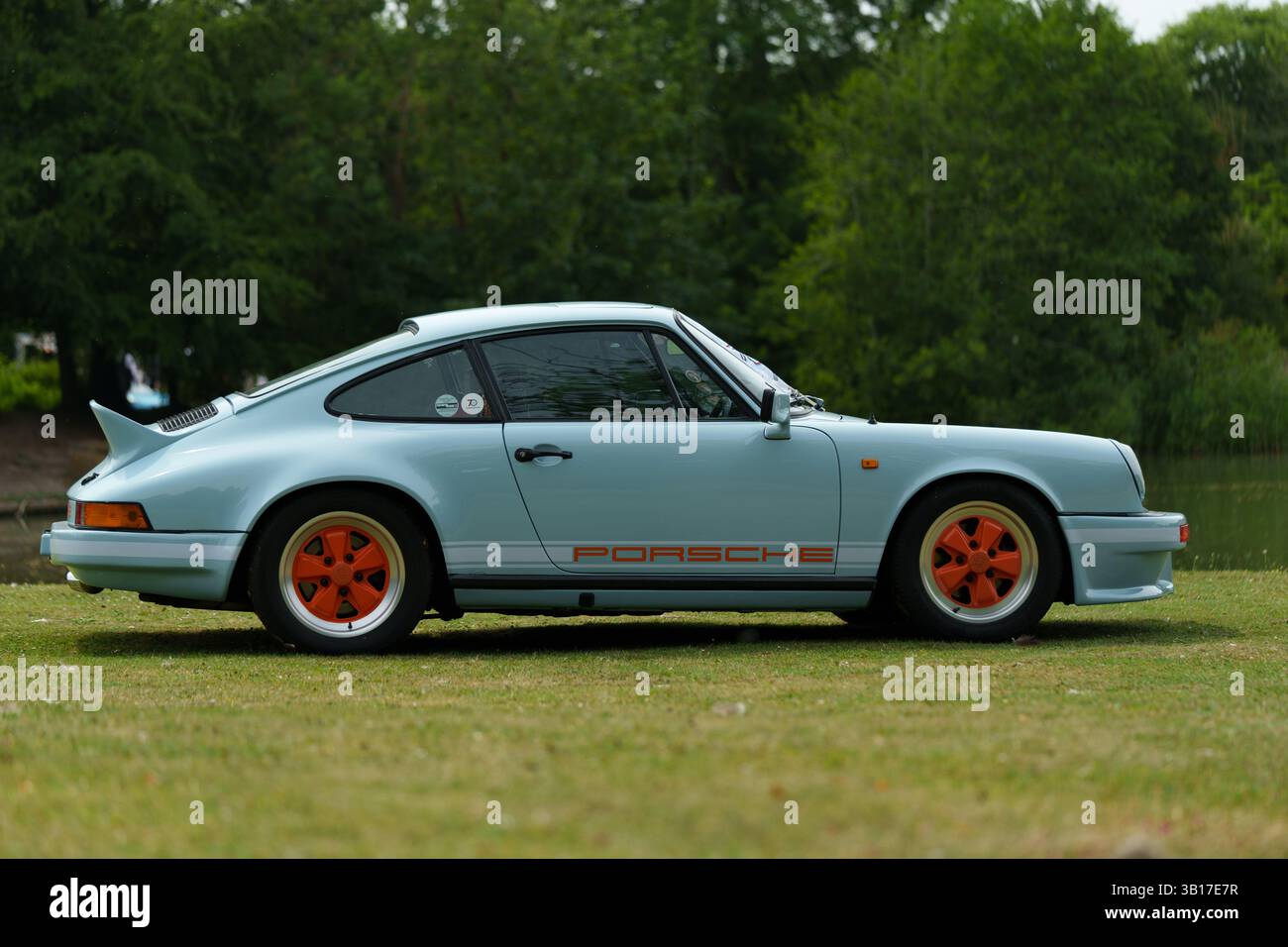 Ein klassischer, hellblauer Porsche 911, der auf Gras geparkt ist, Seitenansicht, mit schlankem Design und orangefarbenen Details. Stockfoto