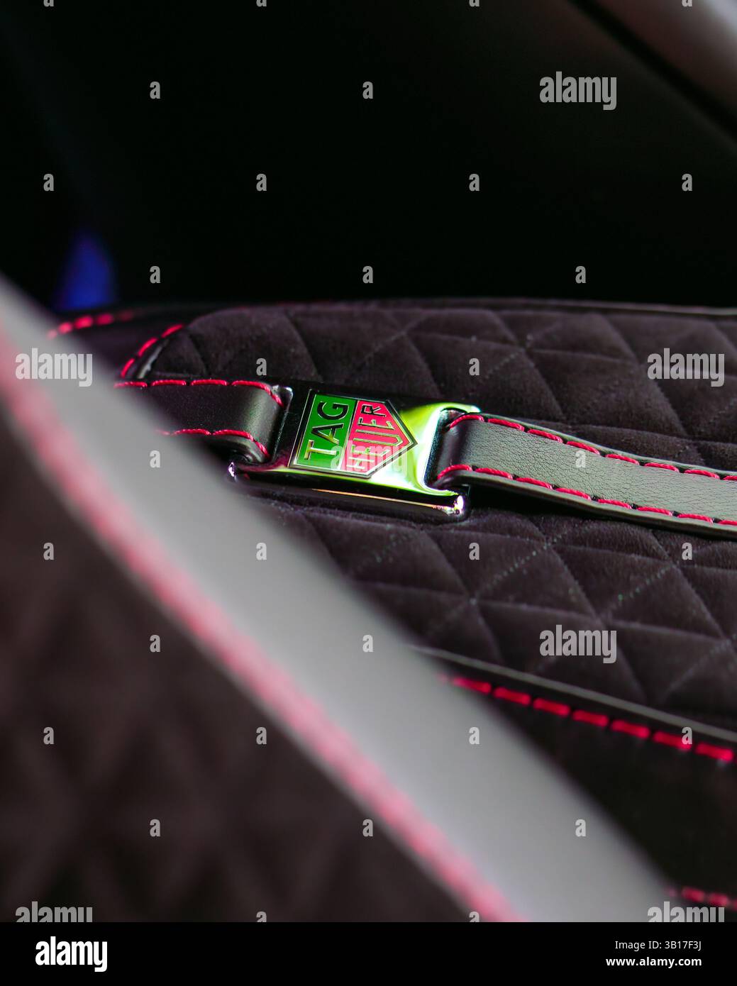 Nahaufnahme eines Sicherheitsgurtschlosses mit TAG Heuer-Logo auf einem gesteppten schwarzen Autositz mit roten Nähten. Stockfoto