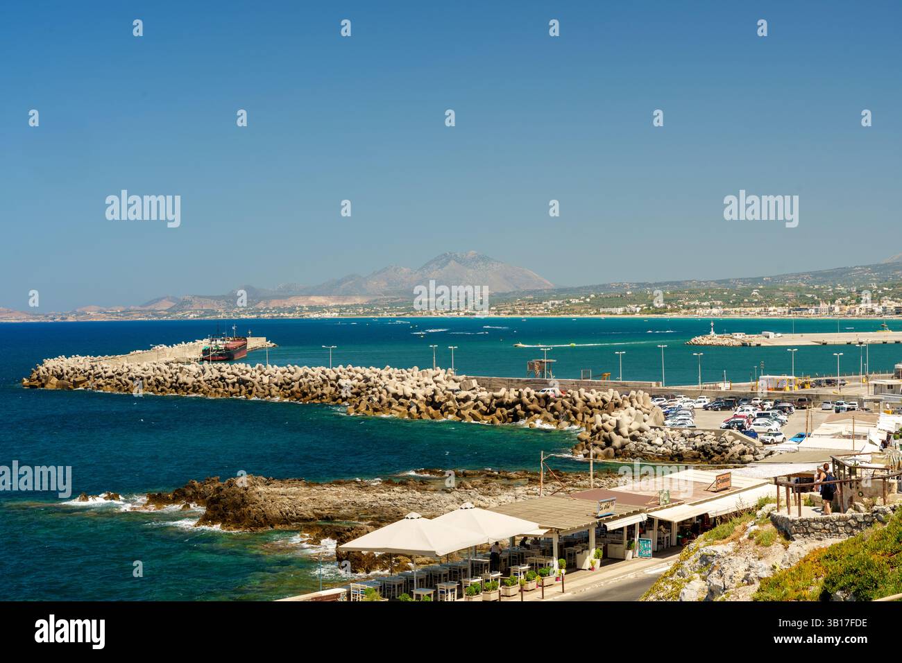 Ein lebhafter Sommerblick auf den Hafen in Hersonissos, Kreta, Griechenland, mit der unverwechselbaren Silhouette des Ida im Hintergrund. Stockfoto