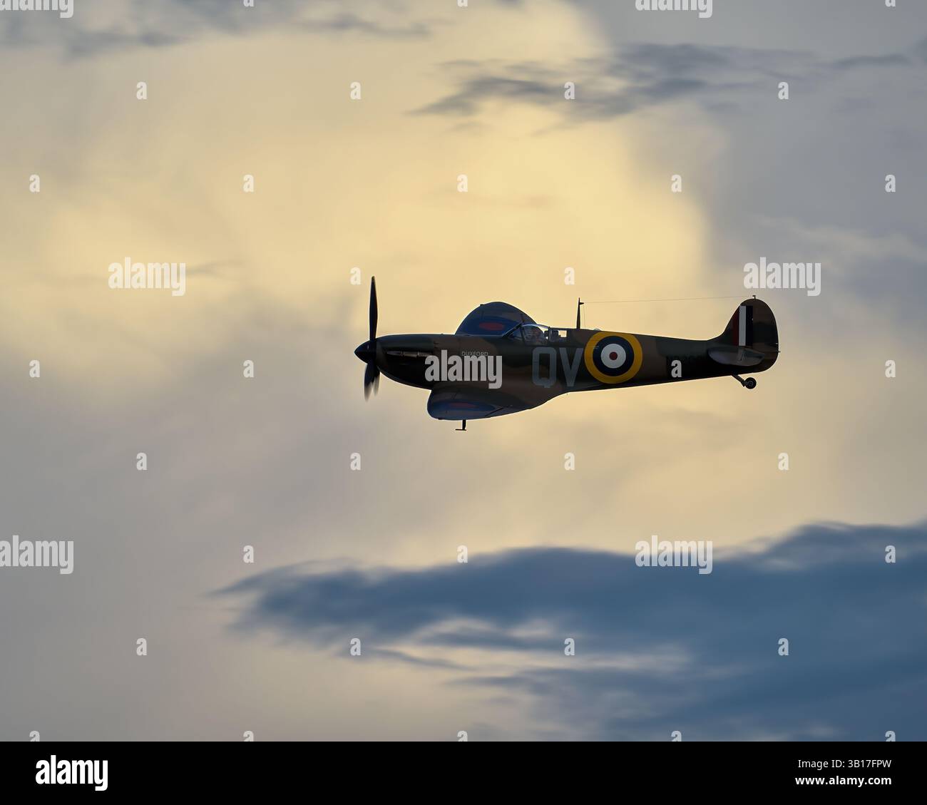 Ein einsitziges Supermarine Spitfire Kampfflugzeug schwingt vor dem Hintergrund dramatischer Wolken während eines Sonnenuntergangs in Duxford, England. Stockfoto