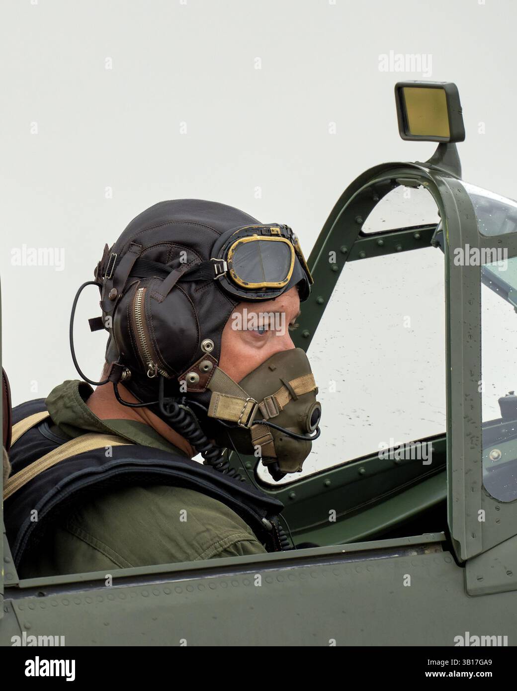 Pilot mit Vintage-Lederhelm und Sauerstoffmaske sitzt im Cockpit eines klassischen Kampfflugzeugs und bereitet sich auf den Flug in Duxford, England, vor. Stockfoto