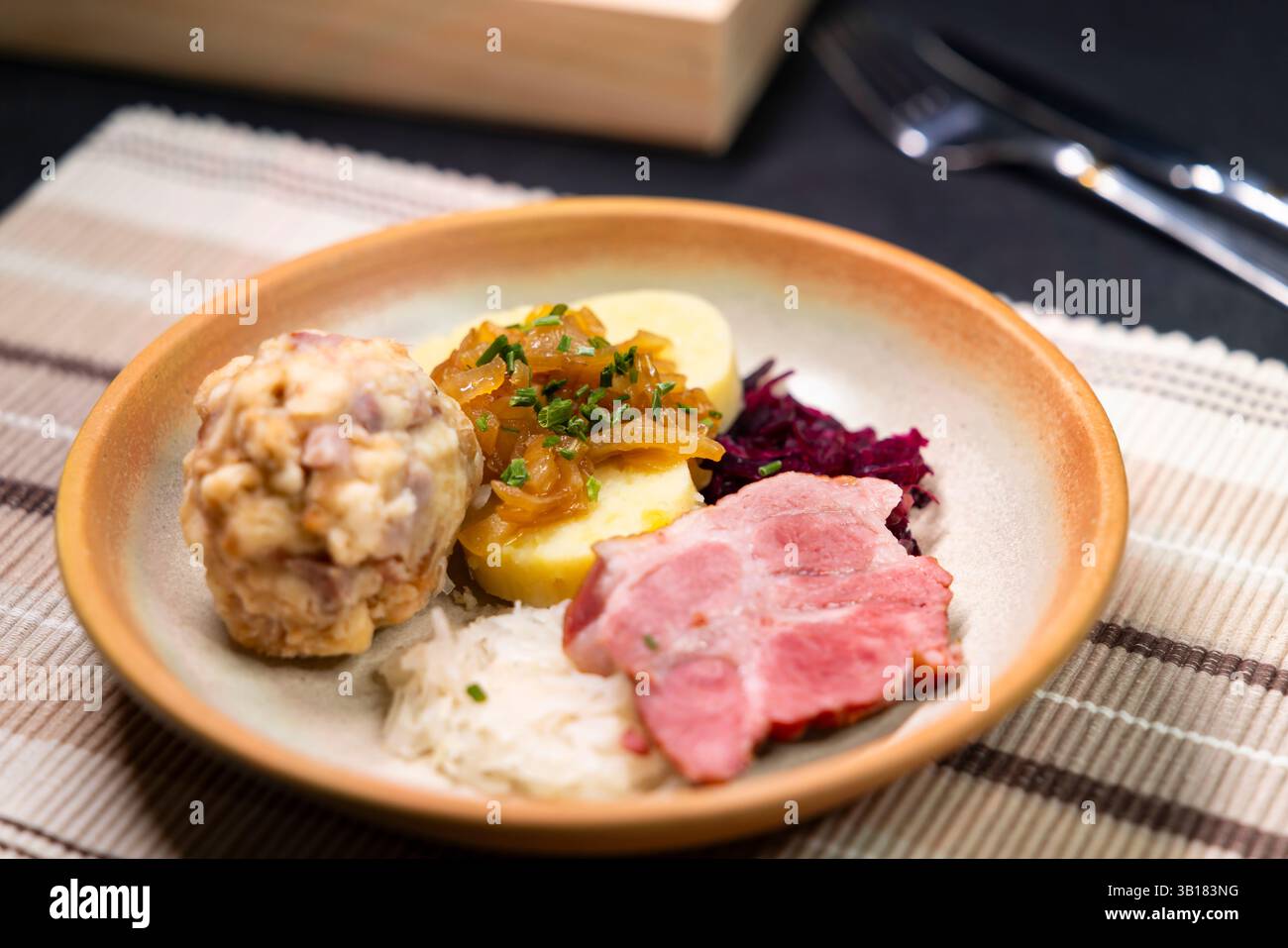 Deftige bayerische Spezialitäten mit Knödeln, gebratenem Schweinefleisch, Sauerkraut und karamelisierten Zwiebeln als Nahaufnahme auf einem Teller Stockfoto