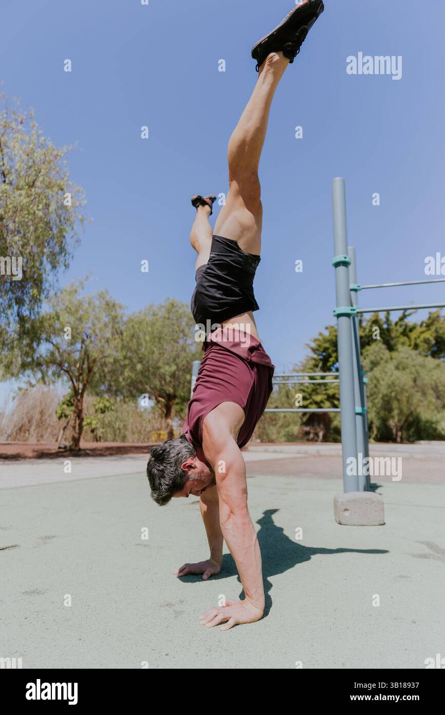 Ein Mann hält während eines Workouts im Freien eine Handstandsposition mit offenen Beinen. Stockfoto
