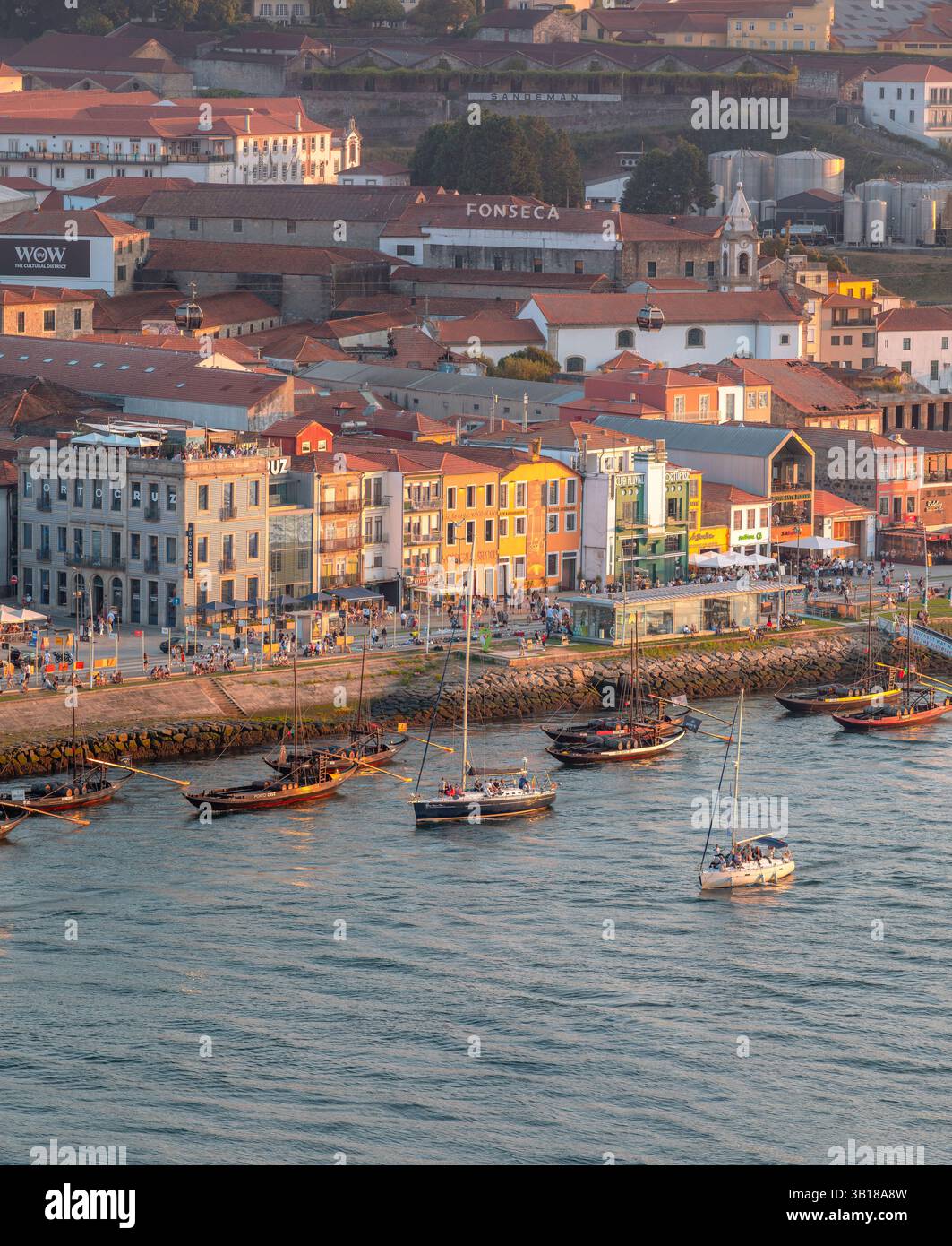 Panoramablick auf farbenfrohe historische Gebäude entlang des Cais de Gaia, Porto, Portugal, mit traditionellen Rabelo-Booten, die auf dem Fluss Douro ankern. Stockfoto