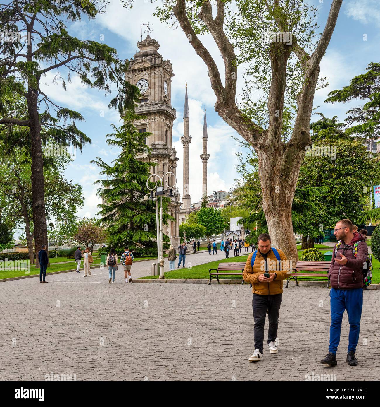 Istanbul, Türkei - 10. Mai 2023: Die Menschen gehen entlang des Weges in der Nähe des Dolmabahce Uhrenturms und genießen die frische Luft und die wunderschöne Umgebung der Dolmabahce Palace Gärten mit hoch aufragenden Bäumen Stockfoto