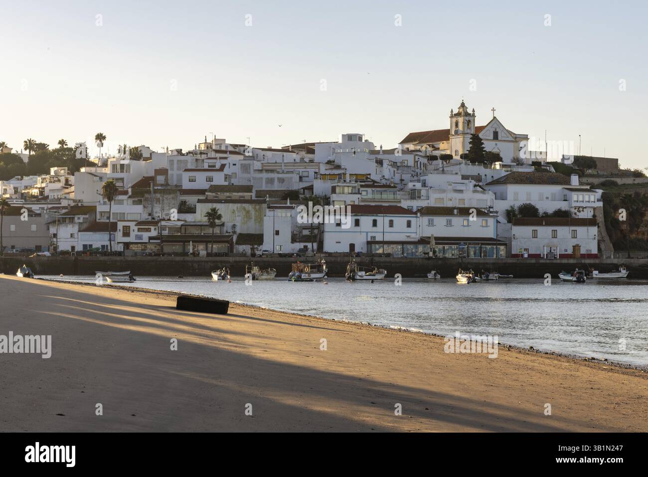 Sonnenaufgang am Atlantik, Skyline eines Fischerdorfes hinter einem Hafen. Sandstrand bei Sonnenaufgang. Landschaftsfotografie in Ferragudo, Portimao, Algar Stockfoto