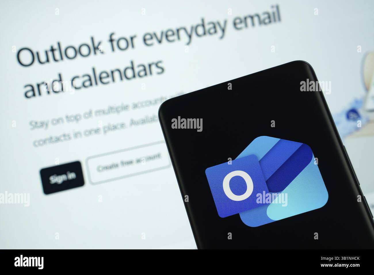Dhaka, Bangladesch – 17. März 2025: Das microsoft Outlook-Logo wird auf einem Smartphone-Bildschirm angezeigt, wobei eine Website mit einem Bestandsdiagramm auf einem Computerbildschirm zu sehen ist Stockfoto