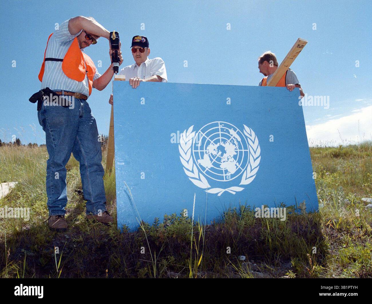 6. Juli 2002 - Kalispell, Montana, USA - drei Männer arbeiten daran, ein Holzbrett zu installieren, das einer Flagge der Vereinten Nationen ähnelt, bevor eine Schießerei in Kalispell, Montana, stattfindet. Viele der Demonstranten fürchten die Kontrolle der Vereinten Nationen über ihr Leben und hassen die Vorstellung einer "neuen Weltordnung". Eine ultrakonservative Gemeinschaft von Waffenrechtlern und Anti-Bundes-Regierungsaktivisten lebt in diesem Teil von Montana. (Kreditbild: © Robin Loznak/Daily Inter Lake/ZUMApress.com) Stockfoto
