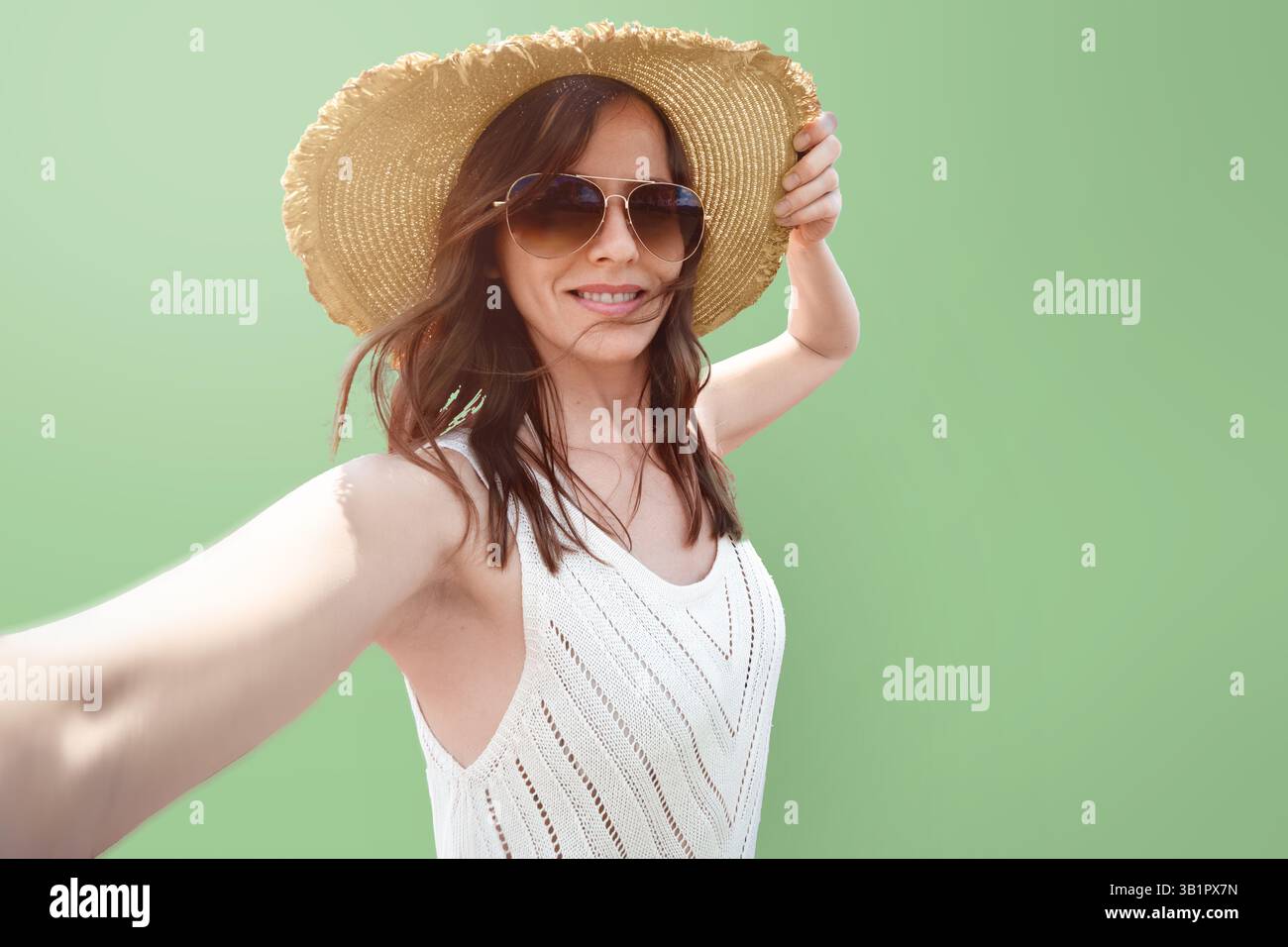 Eine 30- 35-jährige Touristenreisefrau mit breiter Krempe macht ein Selfie vor einem hellgrünen Hintergrundporträt isoliert. Das Konzept von Stockfoto