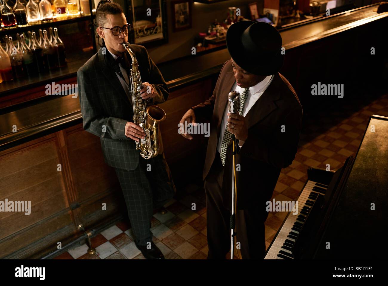 Aufnahmen aus einem hohen Winkel von verschiedenen Musikbands männlicher Saxophonist, die Jazzmelodien spielen, die sich mit der satten, sanften Stimme der schwarzen Sängerin vermischen, während sie im Duett in der Bar, die von warmen Umgebungslichtern beleuchtet wird, Jazz spielen Stockfoto