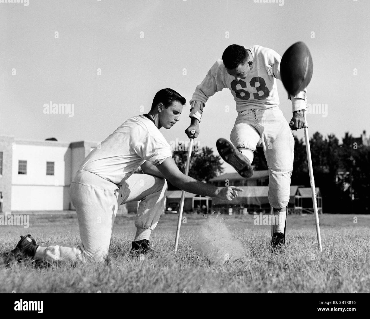 4. September 1953 - Memphis, TN, USA - BILLY GILLESPIE, der vor der Fußballsaison 1952 von Polio betroffen war, ist in der ersten Septemberwoche 1953 wieder in Uniform. Mit Hilfe von Krücken und Zahnspangen an seinen Beinen ist Billy jeden Nachmittag draußen und übt Extrapunkte an der Katholischen High. Hier stillt Billy einen, wie GEORGE WADE ihn hält. (Kreditbild: © The Commercial Appeal/ZUMApress.com) Stockfoto